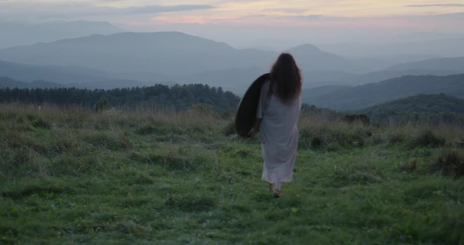 A woman walks in a rural field at sunset