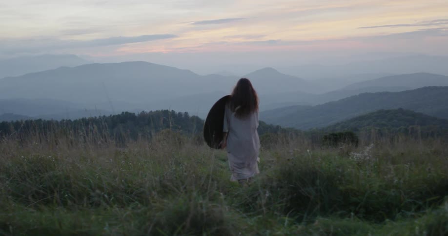 Woman walking in a grassy field near mountains