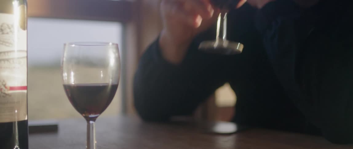 A man is pouring wine into a glass and taking a drink inside in daylight