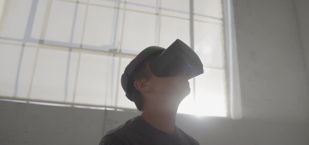 Boy stands next to a window on a sunny day looking through a vr machine