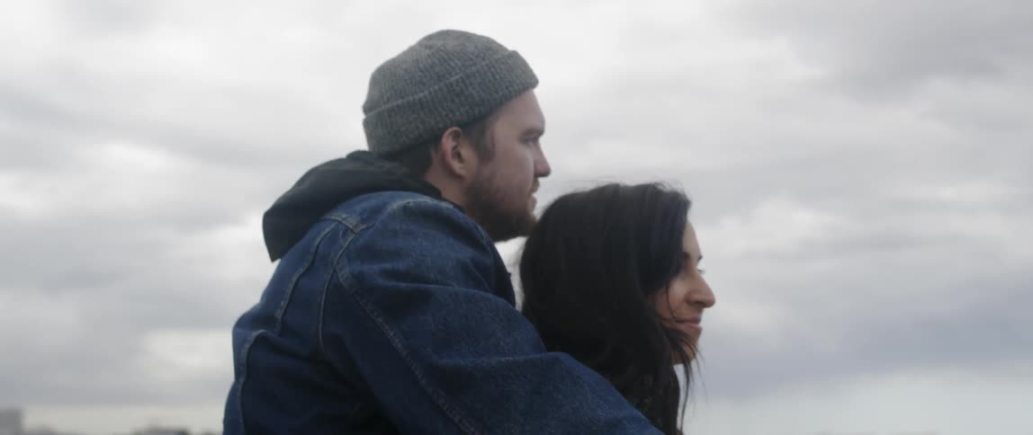 A man and woman enjoy a lake view on a cloudy day