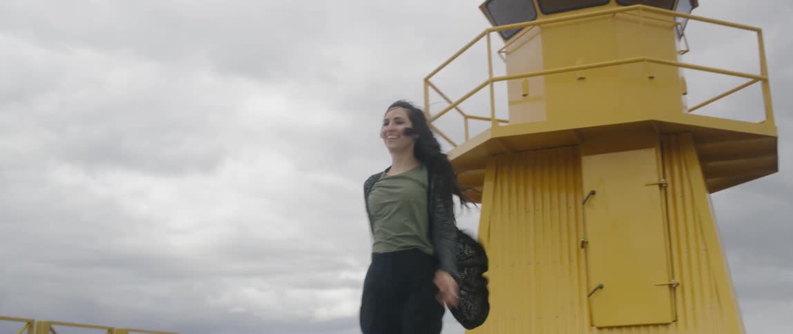 A woman twirls by a lighthouse