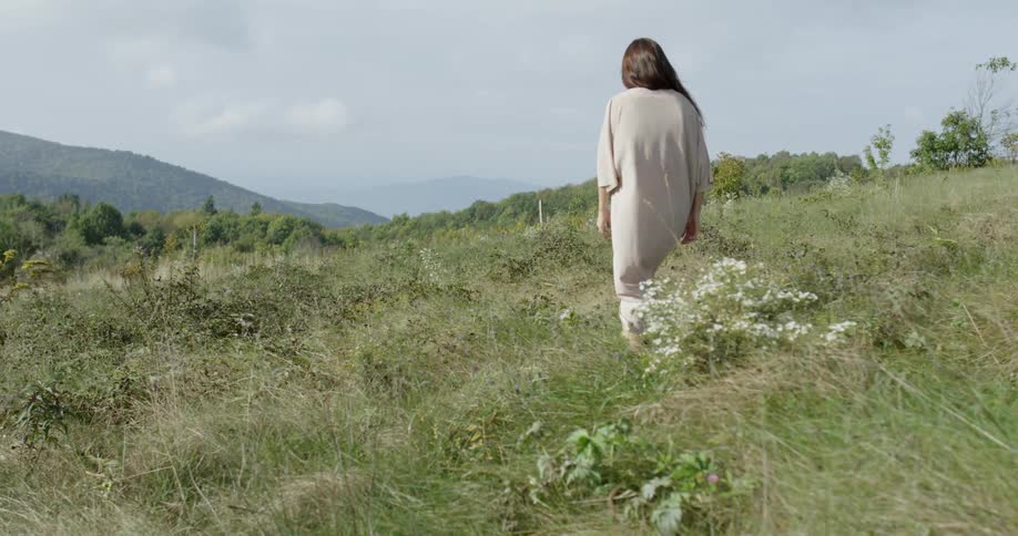 Woman walks in a hilly grassy area on a cloudy day