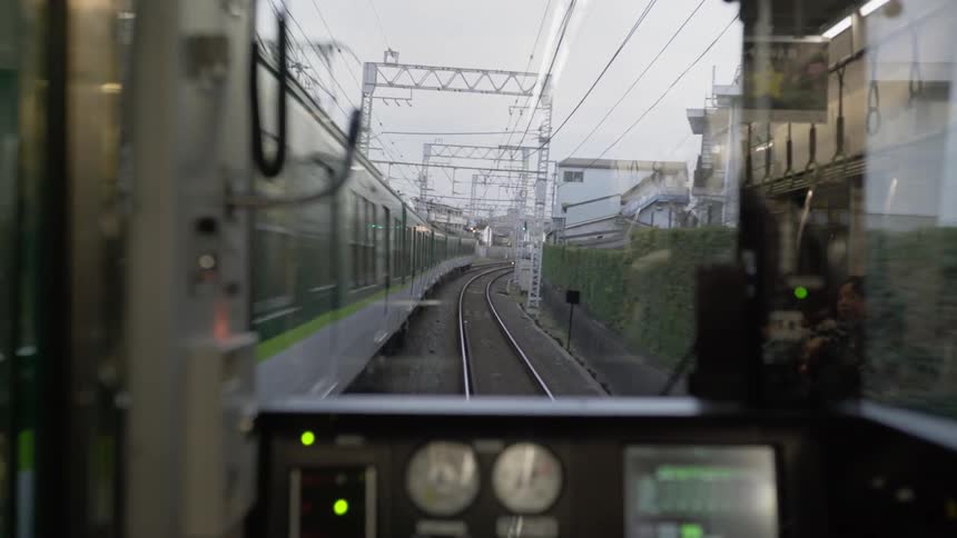 Two trains pass as they travel on tracks through a neighborhood during the day
