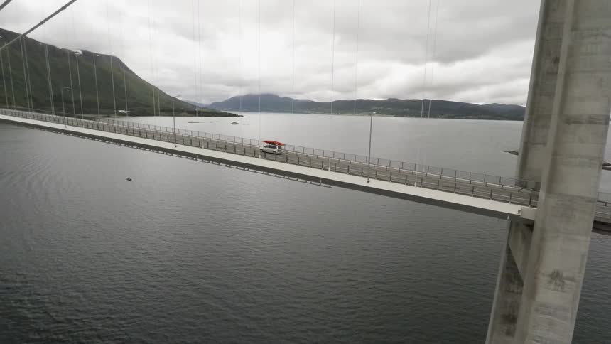 A car driving over a bridge that spans a body of water between two mountainous land masses