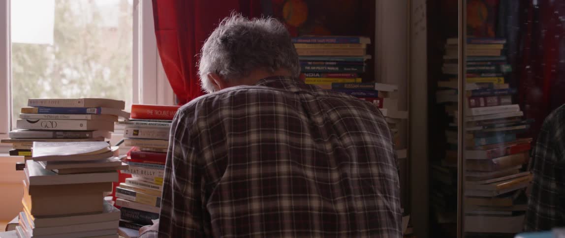 A man sits by stacks of books