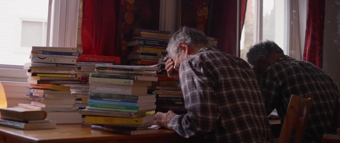 A man works at a desk covered with stacks of books
