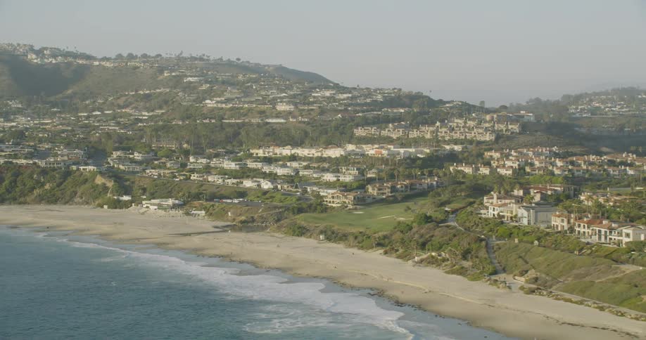 Small waves coming ashore on a narrow beach with houses on the hillsides on a cloudy day