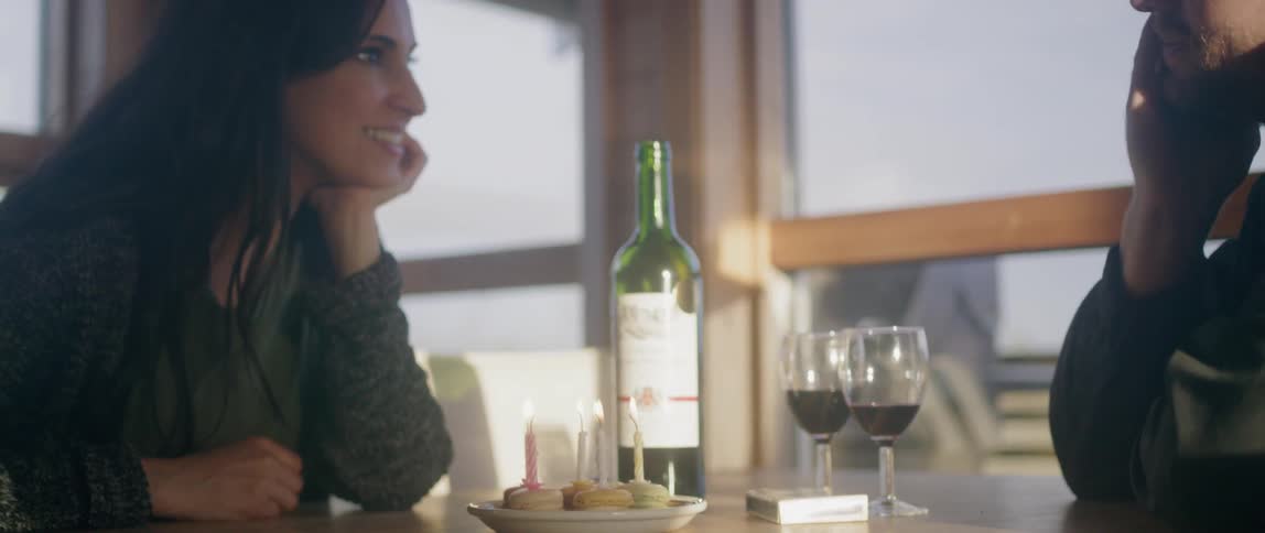 A couple smile at each other over birthday cupcakes and wine