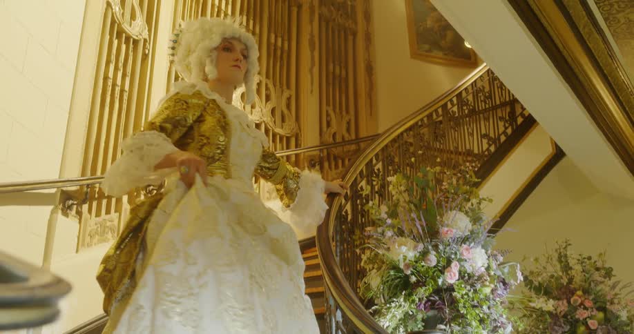 Woman in period costume descends staircase