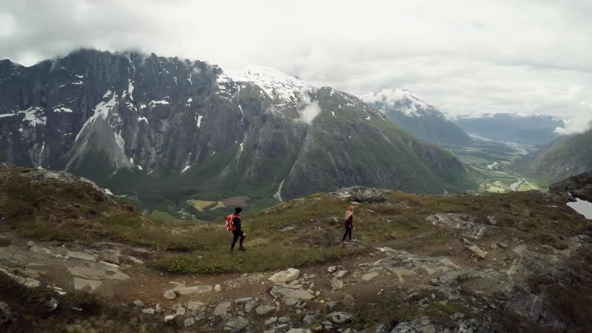 A man and woman hiking in the mountains with snow-capped mountains and a cloudy sky in the background