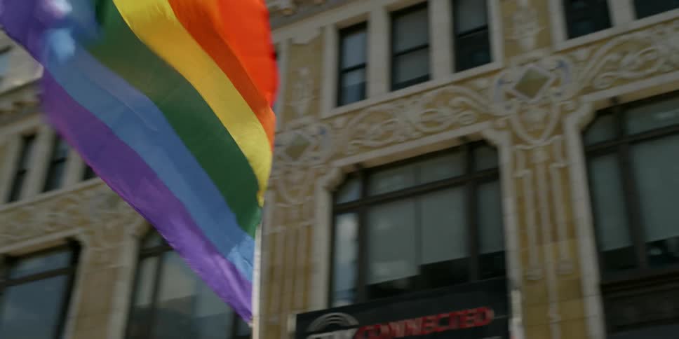 Crowd of people stand in a city and wave rainbow flags