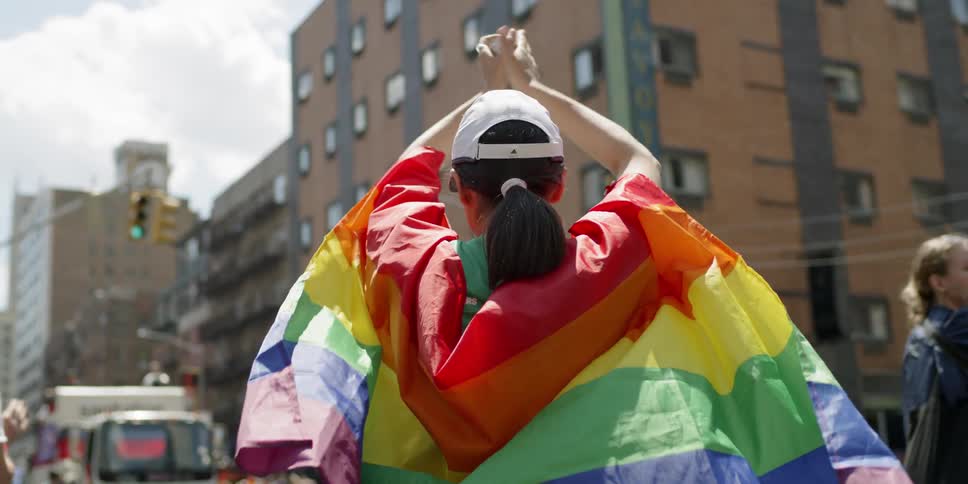 A woman claps in the street wearing a rainbow flag