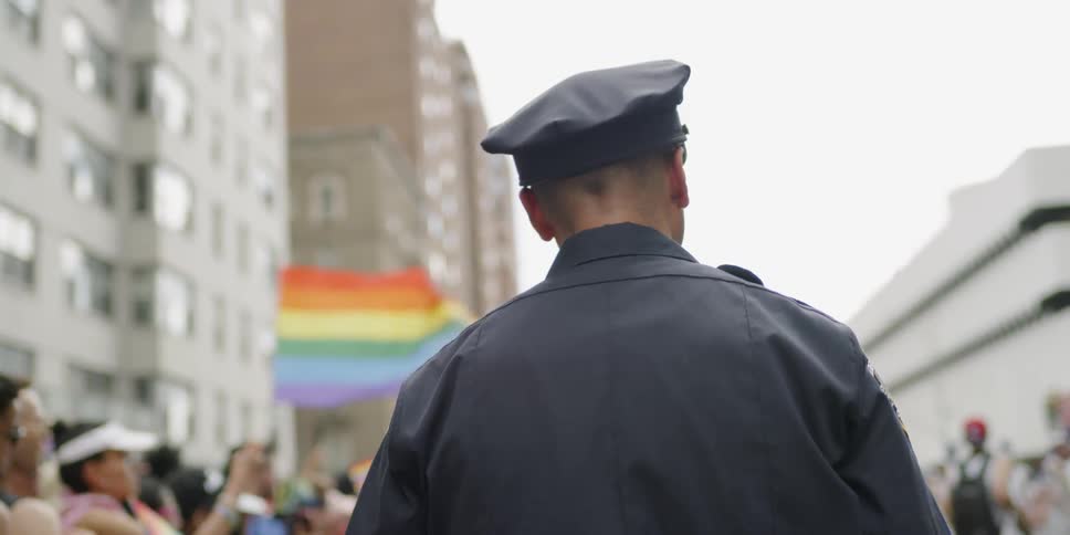 A police officer stands near people gathered for a pride parade in a city