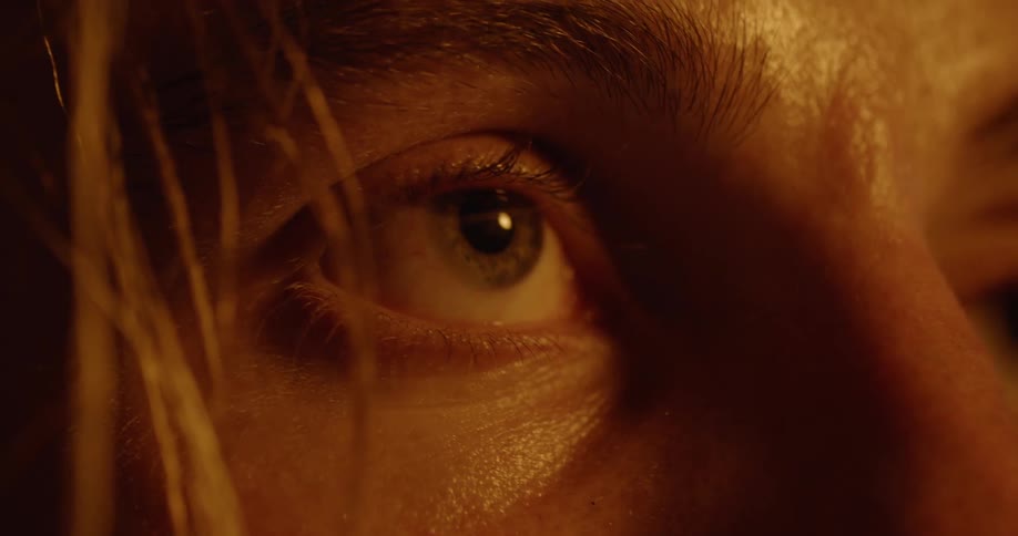A person with blond hair and greenish eyes looks around