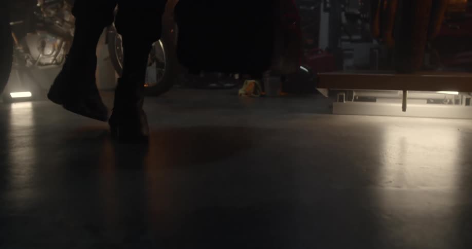 A man is putting down a bag on the floor of a garage in daylight
