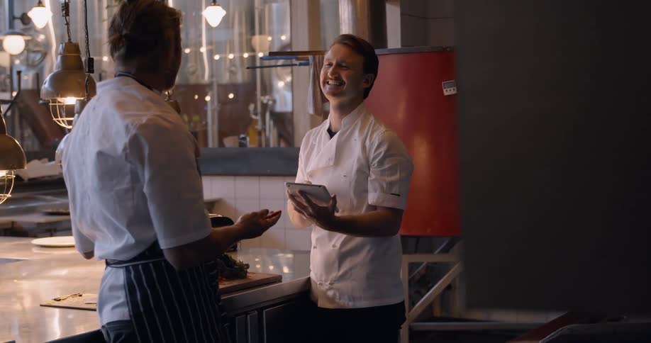 Two men talk and laugh in a restaurant kitchen