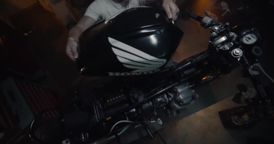 A man puts a gas tank on a motorcycle