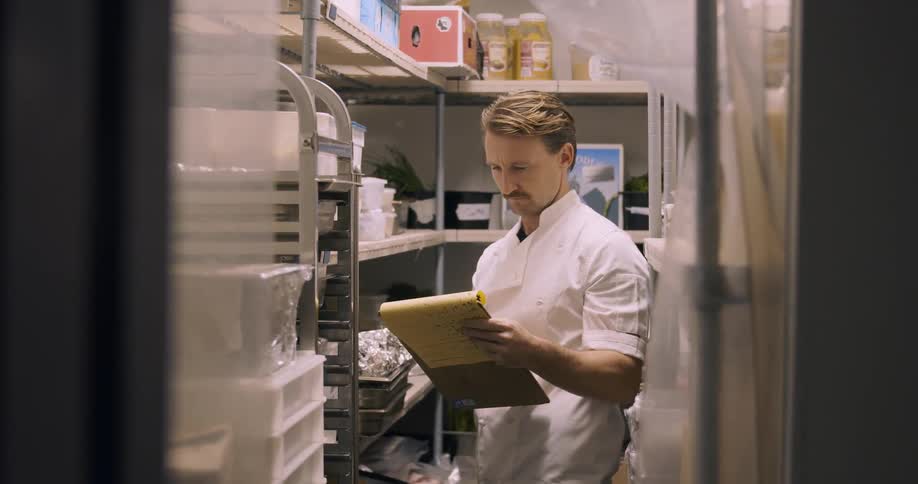 Man stands in a large freezer writing on a yellow notepad