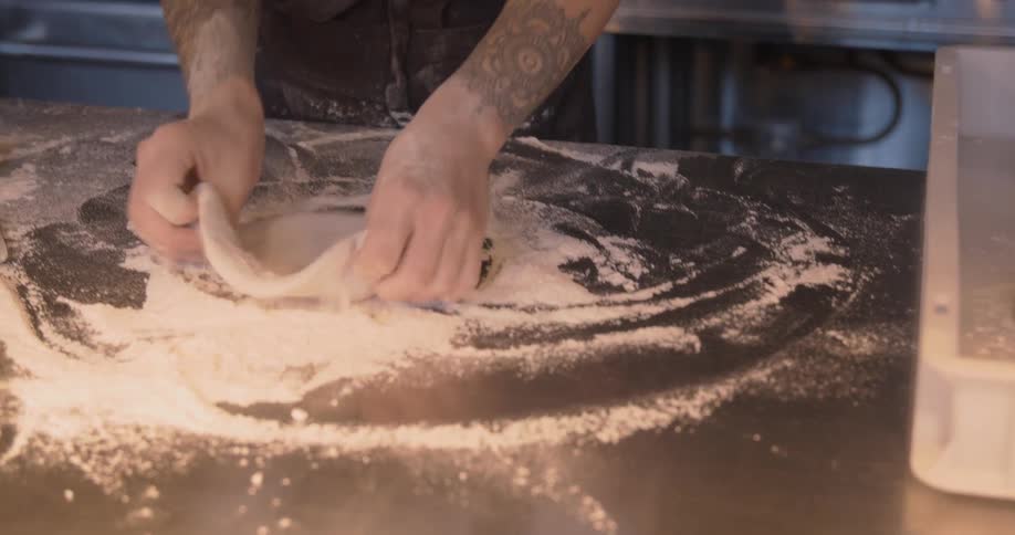 A chef uses flour to help spread a circle of dough on a counter