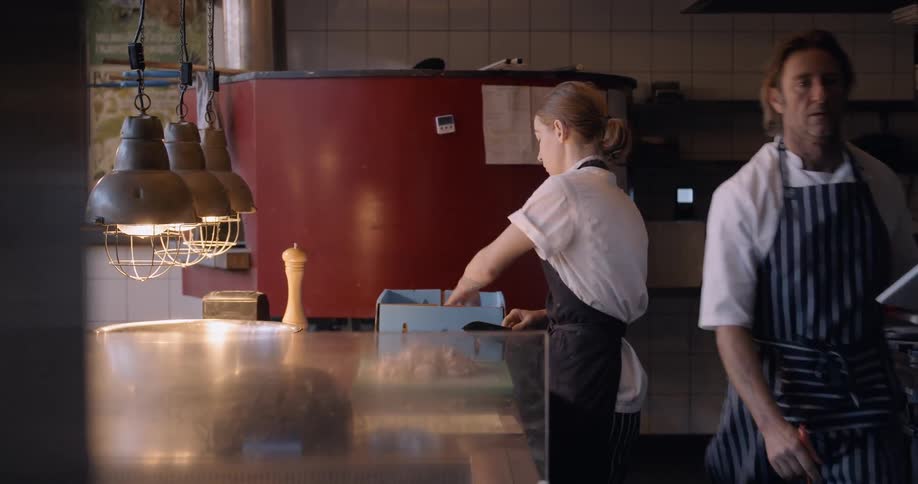 The woman is preparing food as a man walks by