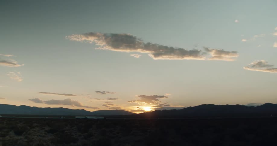 Cars and semi trucks traveling on desolate highway at sunset