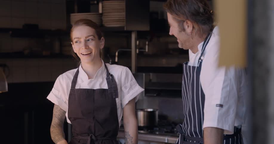 Two chefs talk and laugh in the kitchen