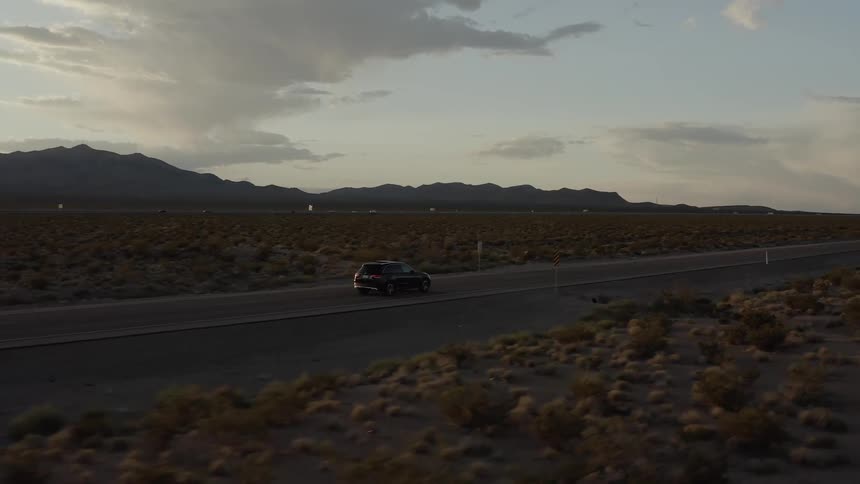 The car drives down the desert road at sunset