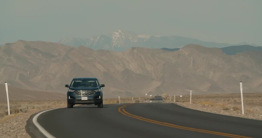 Car drives past camera on highway with mountains in distance