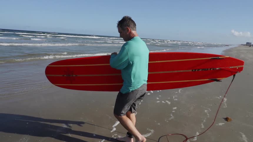 A man walks toward the ocean carrying his surfboard