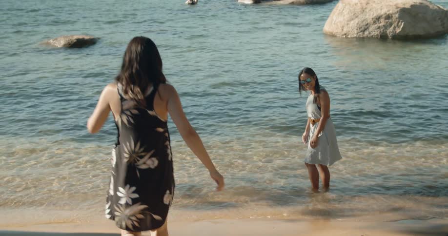 Two women wade in ocean water on a beach