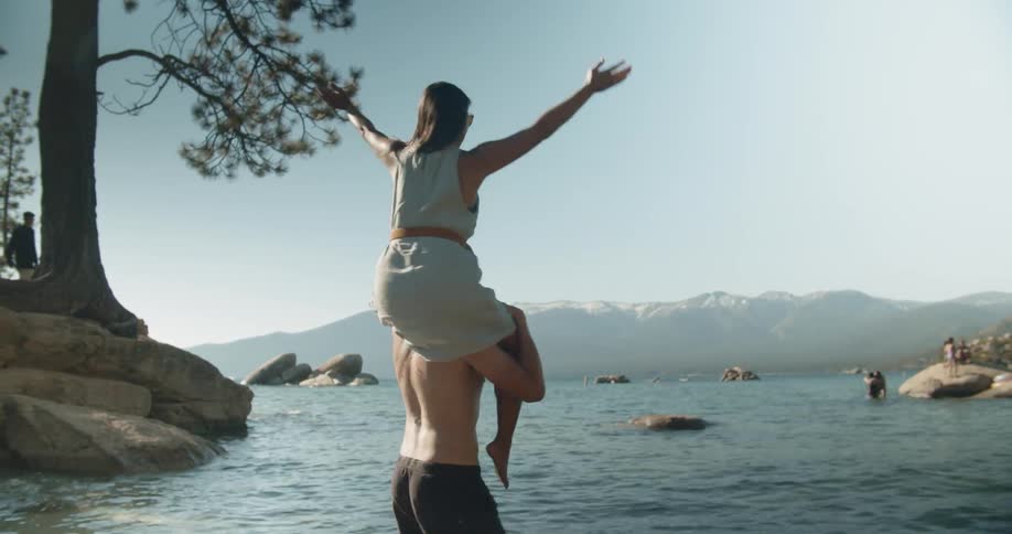 A man spins with a woman on his shoulders in a lake