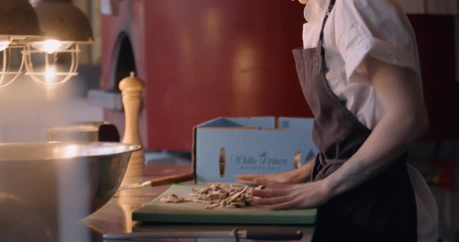 A female chef is working in a restaurant kitchen at dusk
