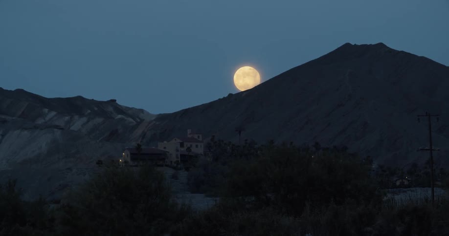 Low full moon rises over a mountain