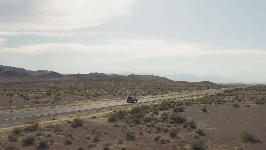 Car drives towards horizon along desert highway
