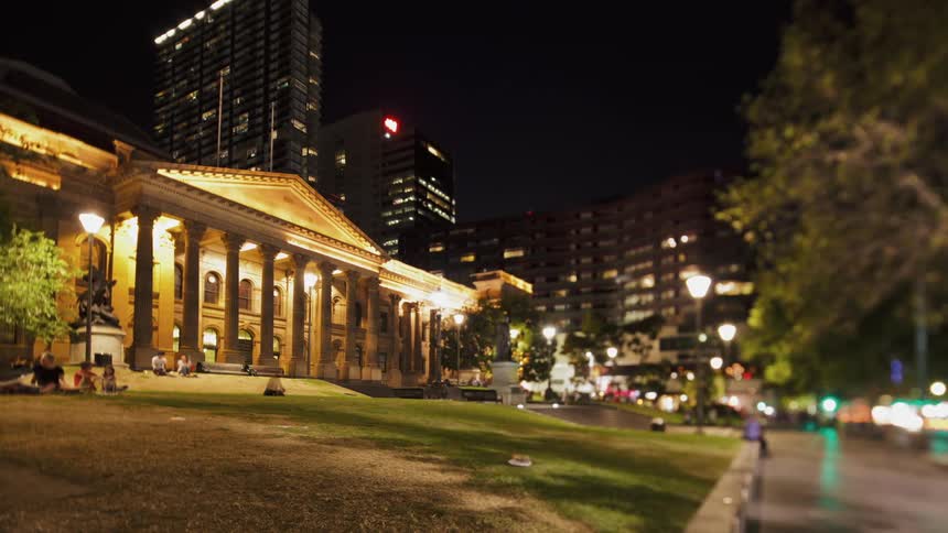 People sit outside a government building in a city at night