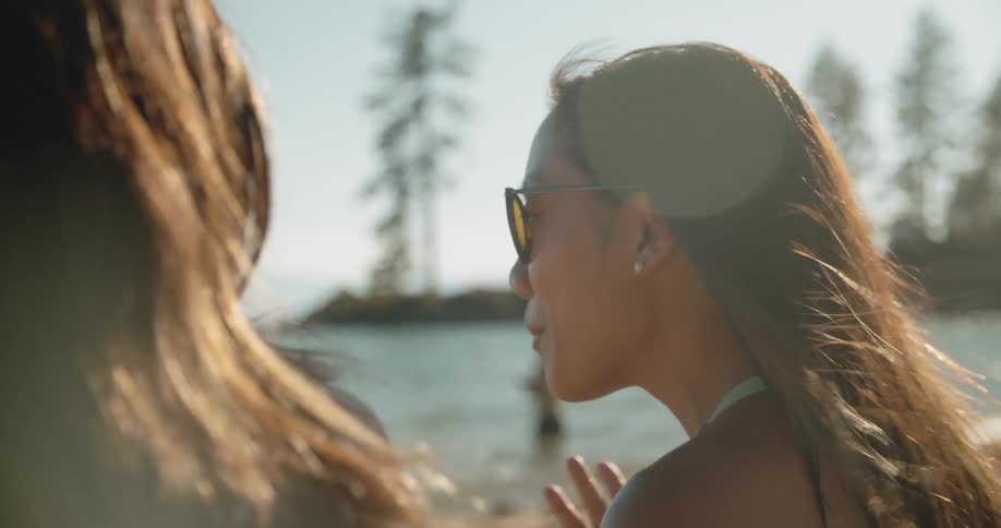 Two women talk on a beach on a sunny day