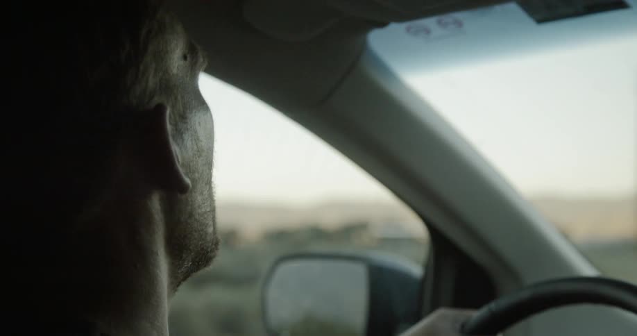 A man drives past a green field