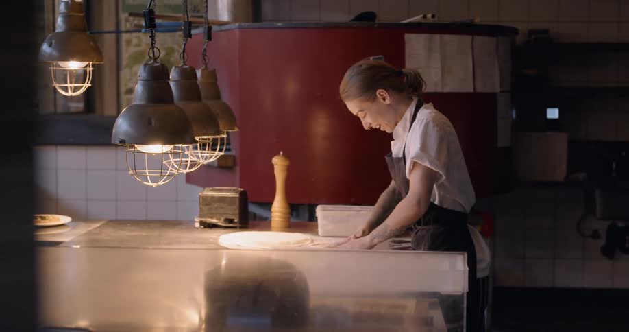 Woman is smiling while making pizza dough in restaurant kitchen