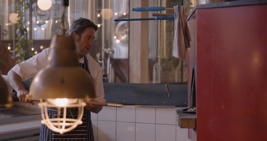 A chef places a pizza into an oven using a long handled paddle