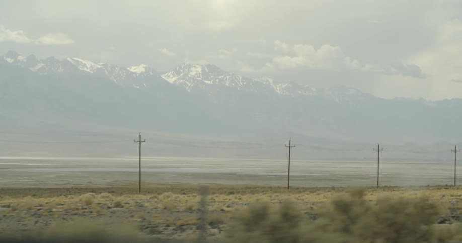 Car drives past view of power lines and snow capped mountains