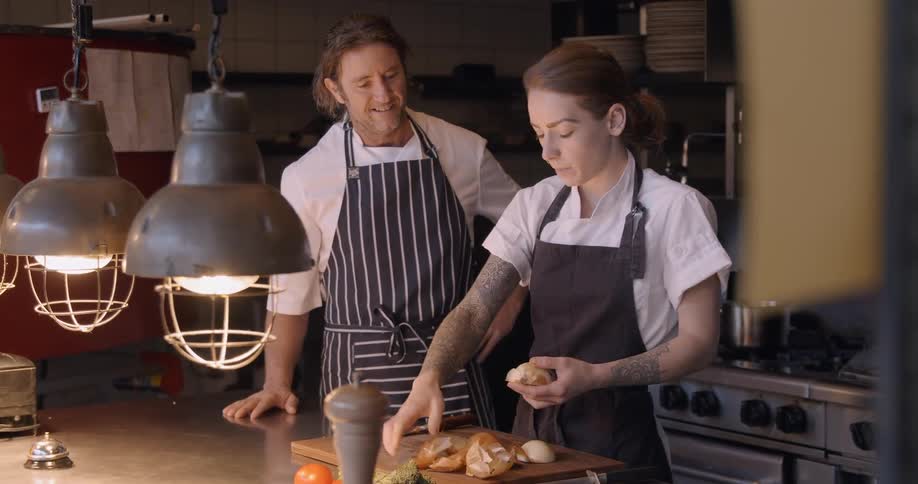 Man talks to a woman who is peeling onions in a restaurant kitchen