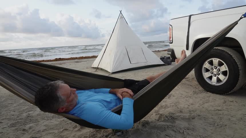 The man is sleeping on the beach in a hammock