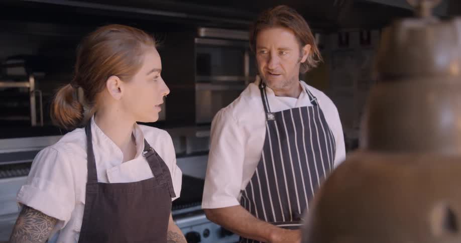 Woman whisks liquid and talks to a man who is chopping vegetables