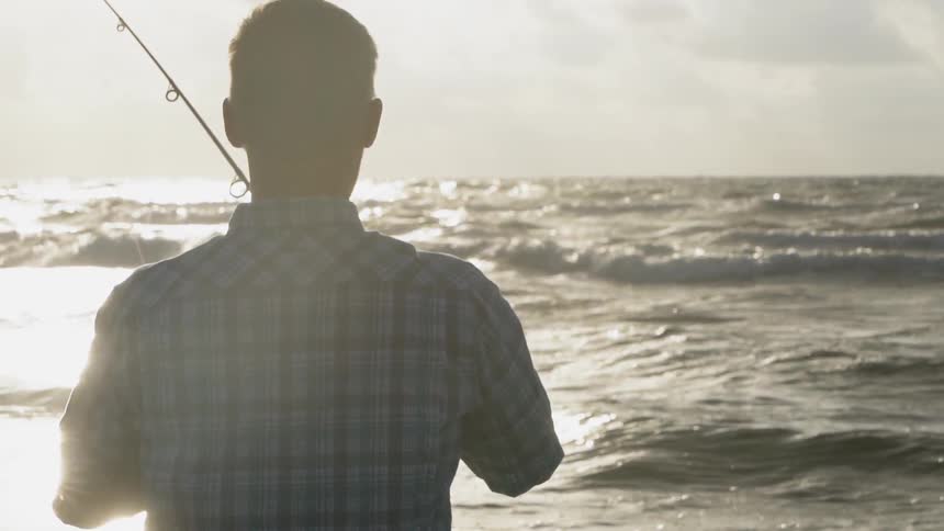 A man is fishing at the beach on a cloudy day