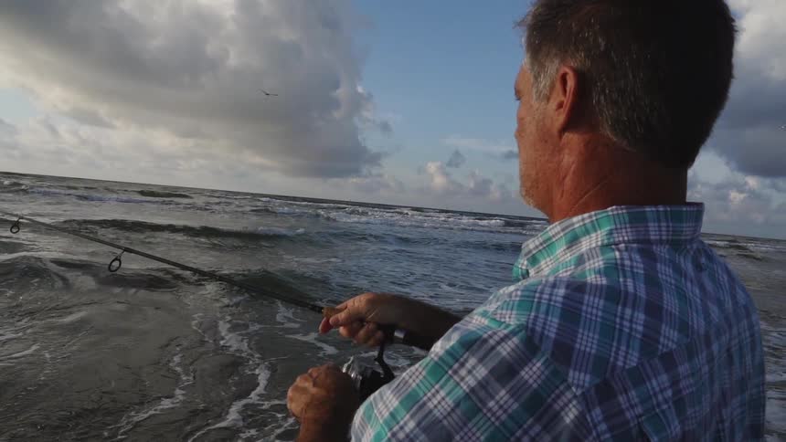 A man fishes on a beach on a cloudy day