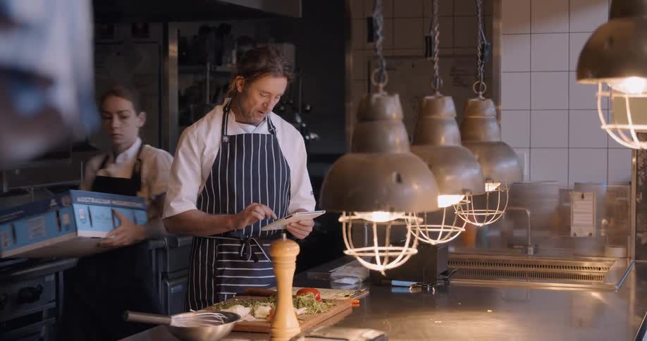 Man types into a tablet looking at food in a restaurant