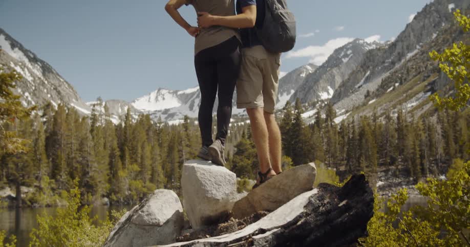 Man and woman stand on a rock kissing and looking out at mountains and trees