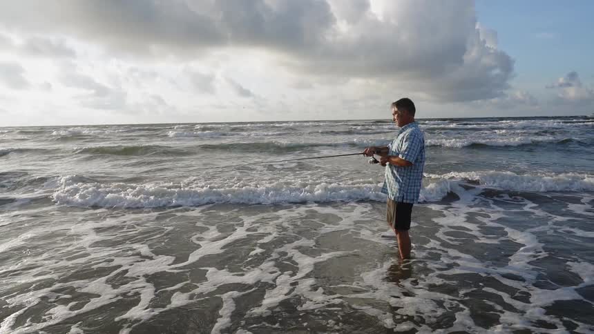 A man fishes on a beach on a cloudy day