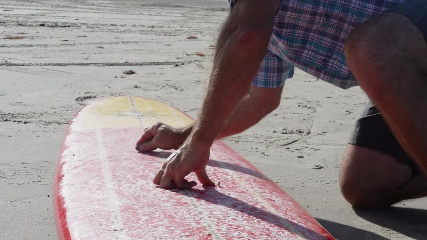 Man waxes his surfboard on the beach